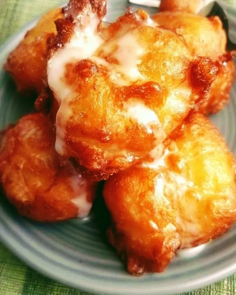 Golden brown peach fritters dusted with powdered sugar on a plate